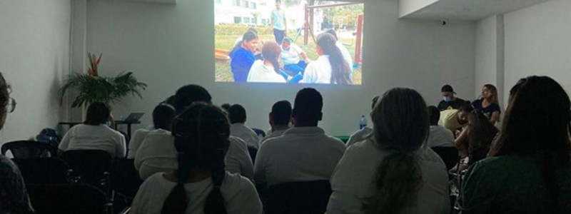 personas en auditorio con luces apagadas ven hacia una proyección