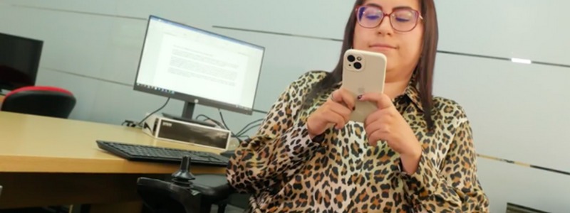 Fotografía: Diana sentada en su silla de ruedas mientras utiliza su celular