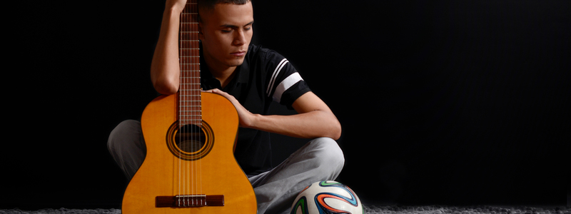 En la imagen: José Quiceno sostiene su guitarra sentado en el suelo junto a un balón de fútbol