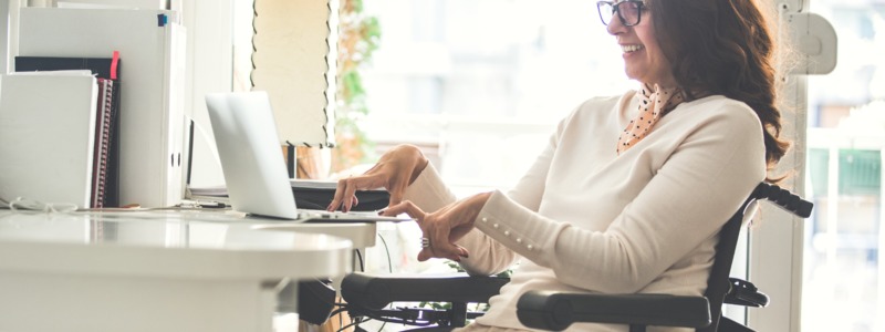 Fotografía: Mujer con discapacidad sonríe frente al computador.