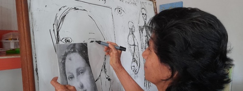 Fotografía: Mujer frente a un tablero dibuja un retrato que sostiene en su mano