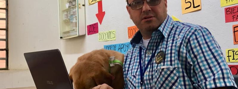 En la fotografía: Hernán Villegas frente a un computador portátil acompañado por su perro lazarillo.